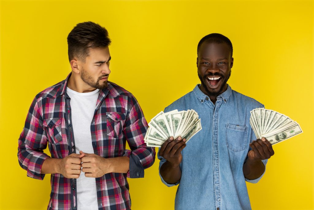 Un homme souriant tenant des billets de banque tandis qu'un autre homme le regarde avec un air contrarié